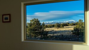 A room with a large window offering a view of a mountainous landscape with snow-capped peaks and a clear blue sky.