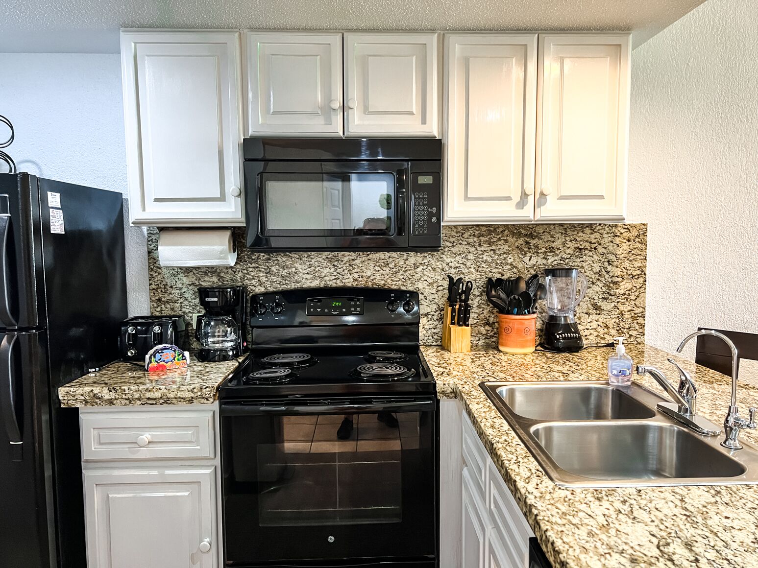 A kitchen with white cabinets, a black stove, a microwave, a sink, and a coffee maker.