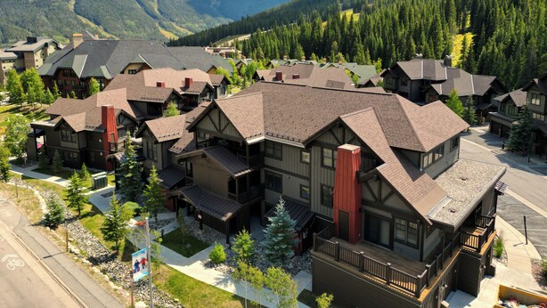 Un ensemble de bâtiments de style rustique, construits en rondins de bois, avec une vue sur les montagnes, comprenant des structures à un ou plusieurs étages, dont certaines sont dotées de balcons et s’organisent autour d’une cour centrale.