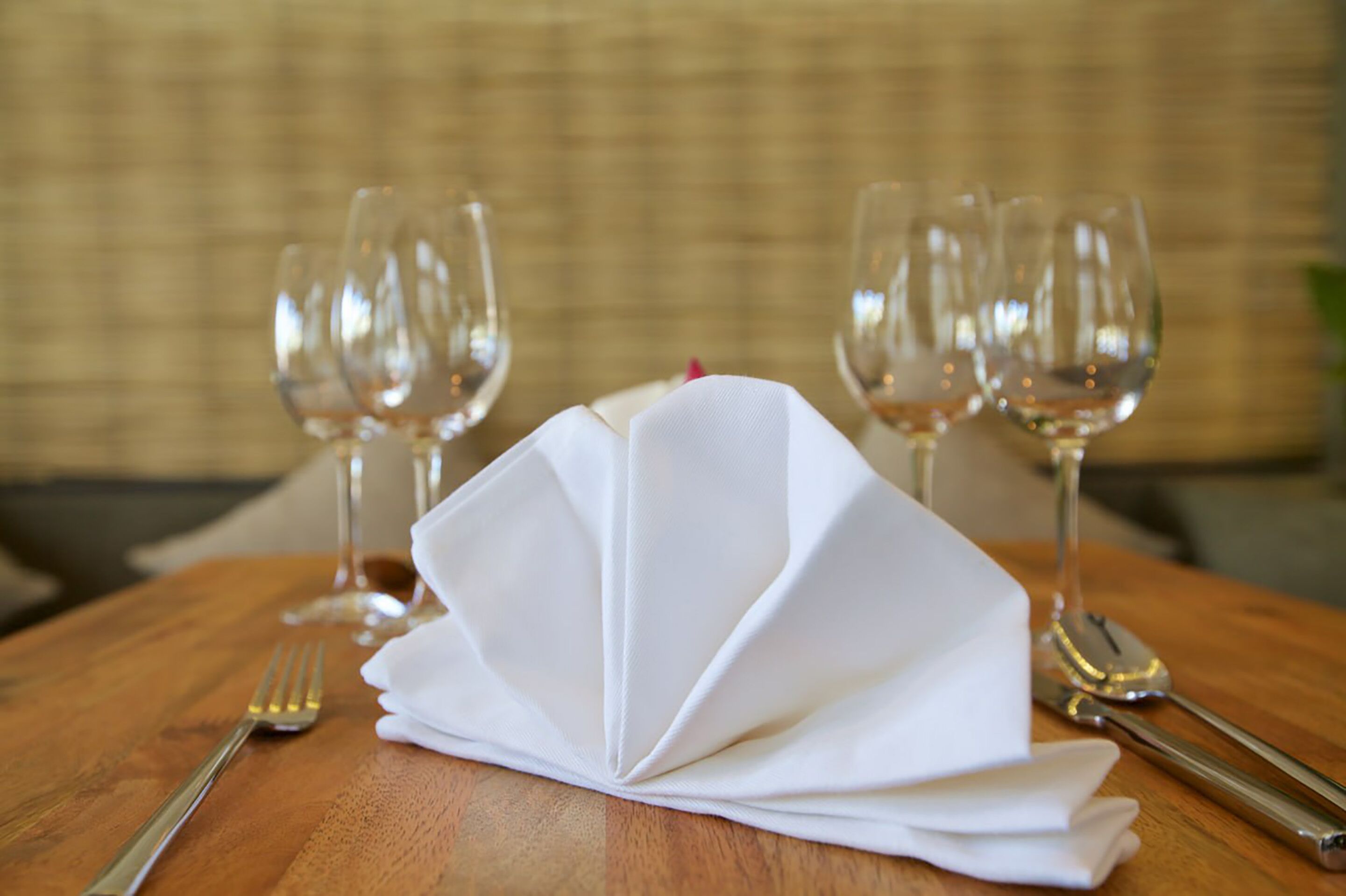 A neatly set dining table with a folded white napkin, two wine glasses, a fork, and a spoon.