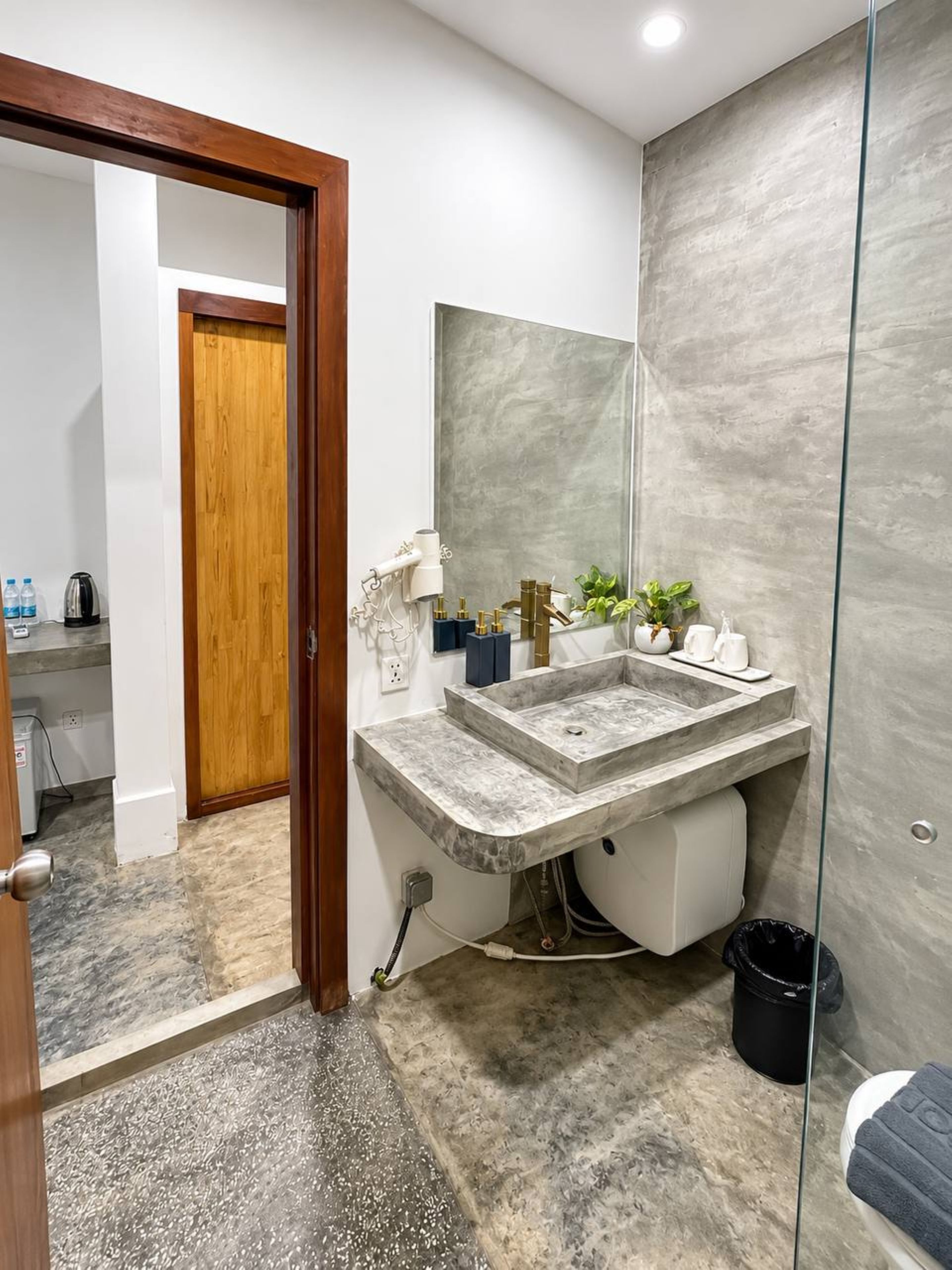 A modern bathroom with a marble sink, a large mirror, and a wooden door leading to a shower area.