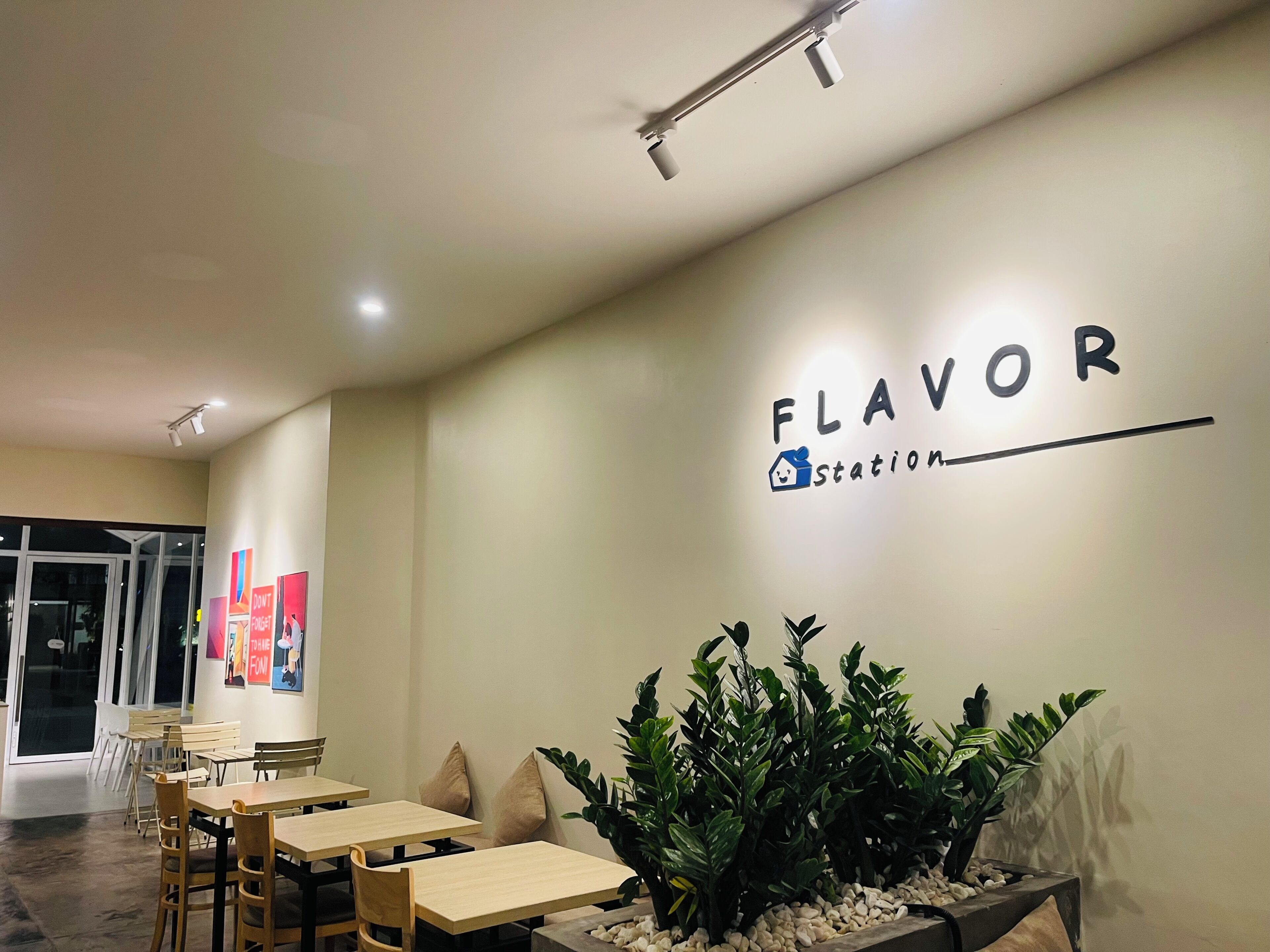 L’intérieur d’un restaurant, avec un panneau indiquant un « coin dégustation », des tables et des chaises en bois, et une grande plante en pot.