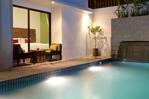 Una habitación de hotel moderna con piscina, una cama con almohadas rojas, una silla verde y una planta en maceta.