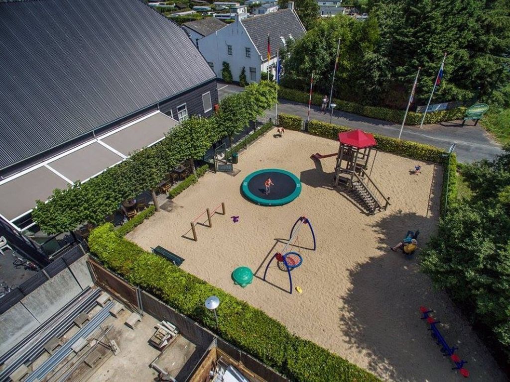 Luchtbeeld van een speelplaats met een trampoline, zandbak en speeltoestellen.