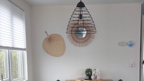 Ein Essbereich mit einem Holztisch, schwarzen Stühlen, einem gewebten Wandbehang und einer Pendelleuchte.