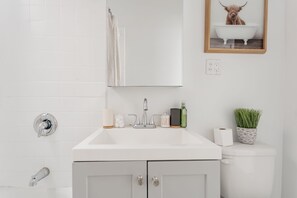 A modern bathroom with a white sink, mirror, and toilet. There is a framed picture of a dog in a bathtub on the wall. - Guest Favorite Getaway in Lakeview Near Wrigley (Chicago)