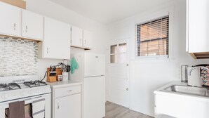 A compact kitchen with white cabinetry, a gas stove, a refrigerator, and a window with blinds. - Guest Favorite Getaway in Lakeview Near Wrigley (Chicago)