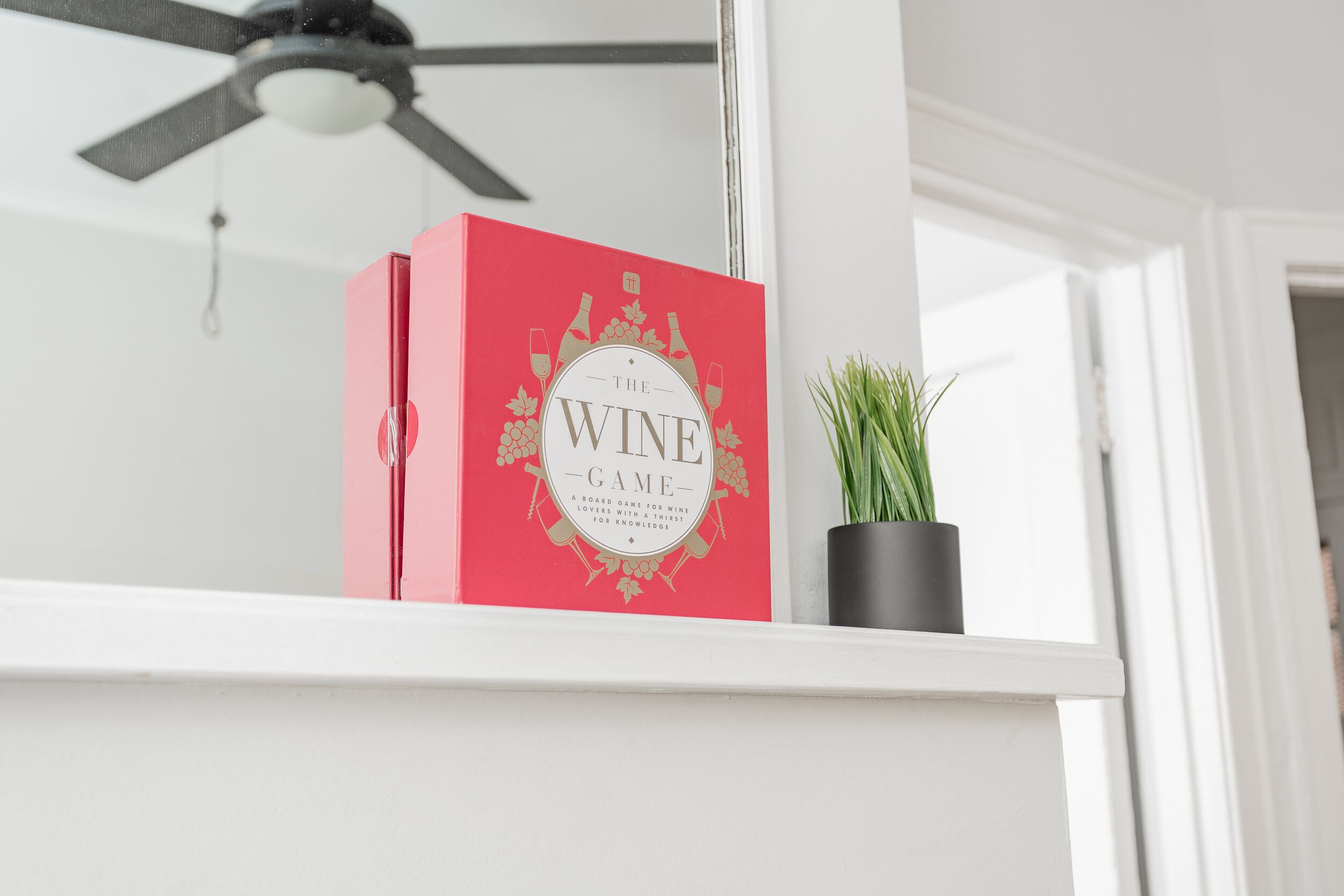 Un libro rojo titulado “The Wine Game” sobre una estantería blanca.