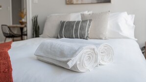 A neatly made bed with white linens and rolled towels, a gray striped pillow, and a white pillow. - Guest Favorite Getaway in Lakeview Near Wrigley (Chicago)