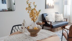 A living room with a round table, a white vase with dried flowers, a wooden bowl with decorative items, a blue sofa, and a framed picture on the wall. - Guest Favorite Getaway in Lakeview Near Wrigley (Chicago)