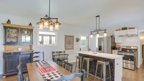 Una cocina con una isla central, taburetes de bar, una mesa de comedor y una lámpara de araña.
