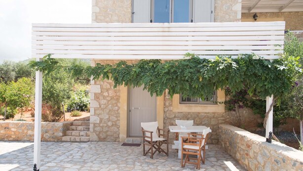 Um pátio de pedra com pérgola coberta por vegetação, mobiliário de exterior e um muro de pedra.