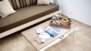 Uma cama com colchão marrom e almofadas listradas, uma mesa de centro de madeira com revistas, um controle remoto, um copo d'água, uma caneca e uma pequena planta.