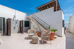 Um terraço no telhado com mobiliário de vime, uma escadaria e plantas em vasos.