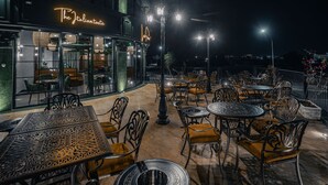 Un área de comedor al aire libre con mesas y sillas, un letrero de neón que dice "The Italian Taste", y vista panorámica de la ciudad de noche.