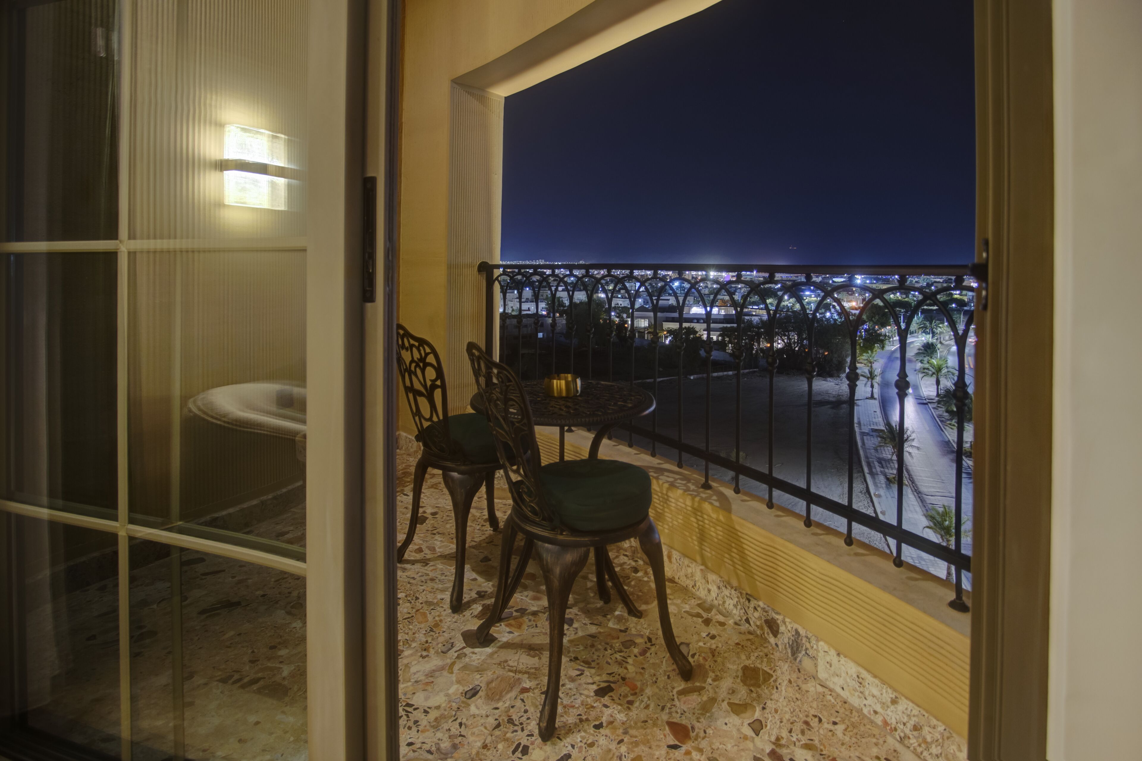 Un balcon offrant une vue sur le paysage urbain nocturne, avec une balustrade et deux chaises.