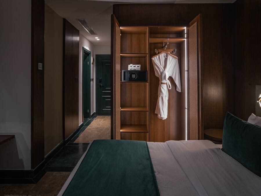 A hotel room with a bed, a robe hanging on a rack, a walk-in closet, and a vanity with a mirror.