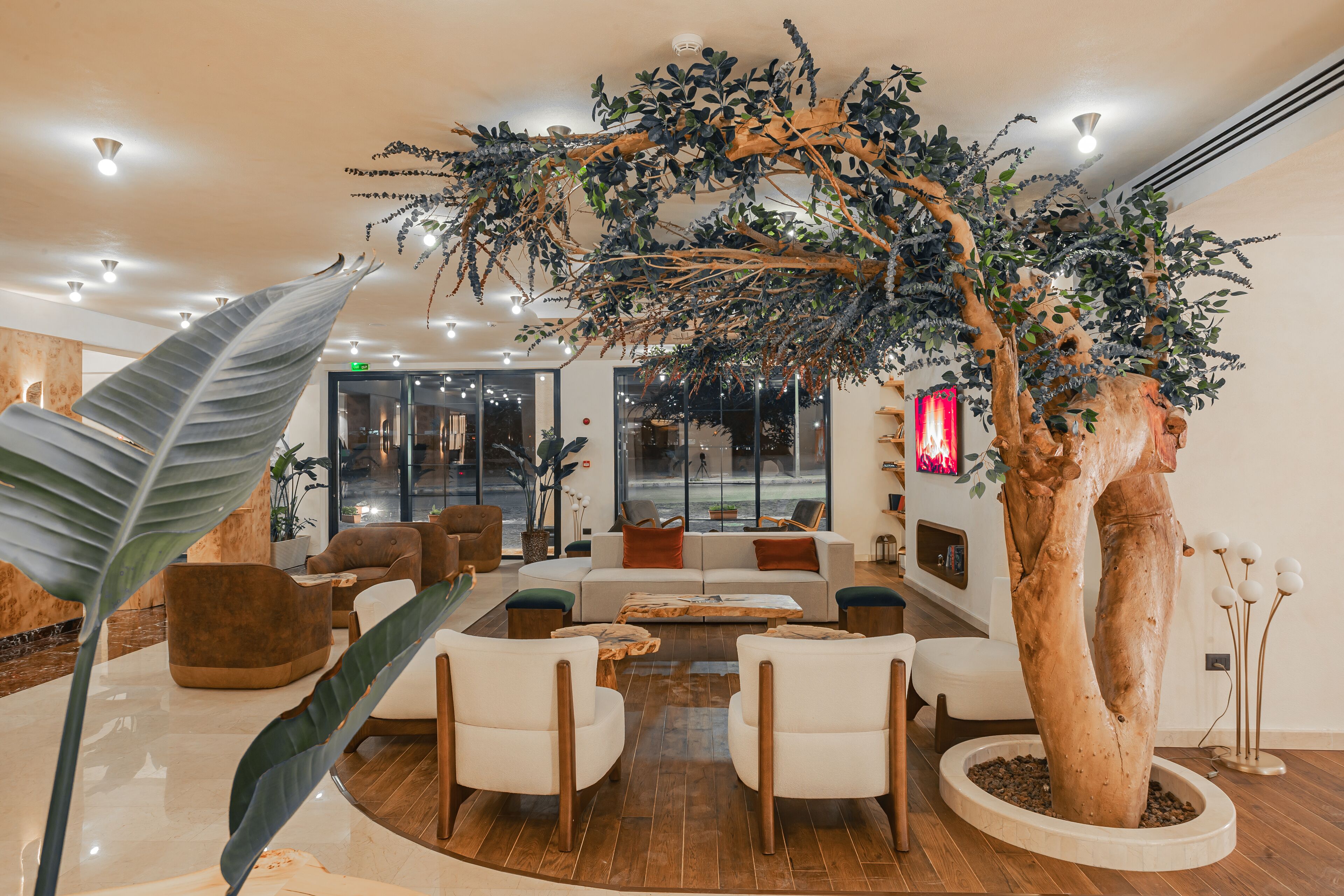 A modern lobby with a large artificial tree, comfortable seating, and a wooden floor.
