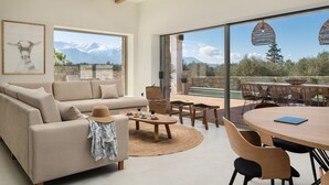 Een moderne woonkamer met een bank, salontafel en een eethoek. Er is een groot raam met uitzicht op de bergen.