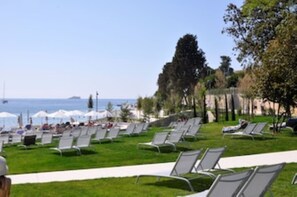 A beachside area with rows of sun loungers and umbrellas, a clear view of the sea, and a grassy lawn. - Alessia Apartment 02 (Rovinj)
