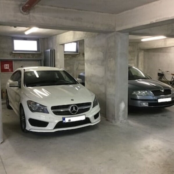 A parking garage with two parked cars, concrete pillars, and fluorescent lighting. - Alessia Apartment 02 (Rovinj)