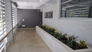 Un pasillo con una larga jardinera con plantas, una barandilla de cristal a la izquierda y una ventana a la derecha.