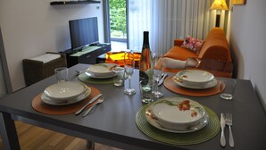 Una mesa de comedor dispuesta con platos, vasos y cubiertos, una televisión y un sofá al fondo.