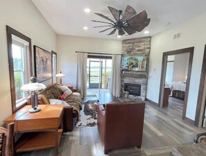 Relax in this inviting living space with a stone fireplace, comfortable seating area, and large windows offering a view of the outdoors.