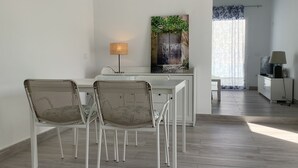 A modern kitchen with white cabinetry, a dining area with wicker chairs, and a view of a garden through a window. - Penthouse between sea and mountains (CN)