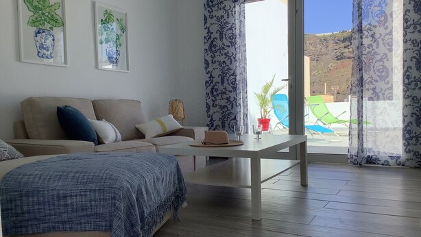 A modern living room with a sofa, a coffee table, and a bed. There are two framed artworks on the wall, a window with curtains, and a view of the outside. - Penthouse between sea and mountains (CN)