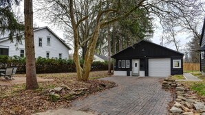 A residential driveway leading to a black garage with a white door, surrounded by trees and a stone wall.