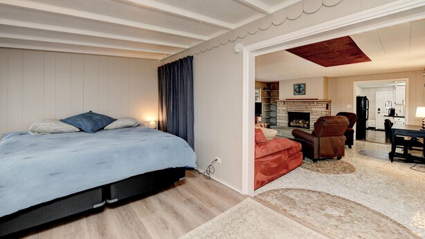 A bedroom with a bed, a red armchair, a fireplace, and a dining area with a table and chairs.