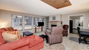 A living room with a fireplace, a television, and a kitchen visible through an open doorway.