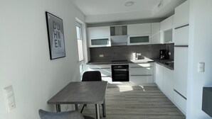 Et moderne køkken med hvide skabe, indbygget ovn og et spiseområde med et bord og stole.