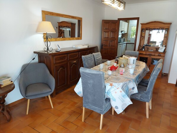 Un coin repas avec une table en bois, des chaises à revêtement gris, une lampe et un miroir au mur.