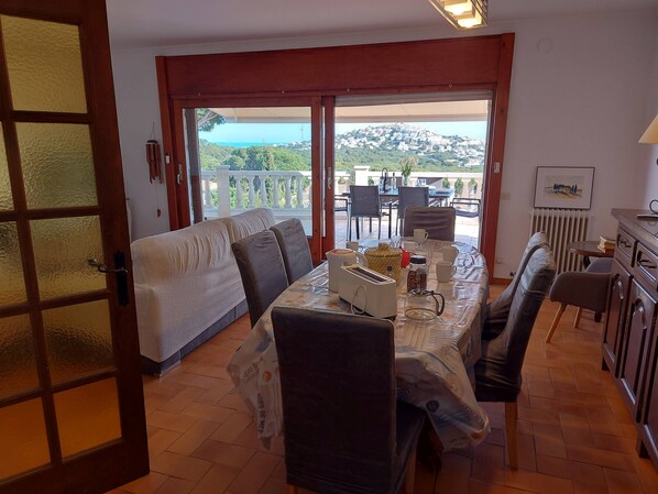A dining area with a table set for two, a sofa, and a view of a balcony with outdoor seating. - Spacious villa with stunning sea views (L'Escala)