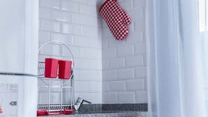 Una cocina con paredes de azulejos blancos, un guante de cocina rojo y blanco a cuadros, y una rejilla de metal con recipientes rojos.