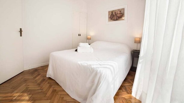 Un dormitorio ordenado con cama, lámparas de noche y suelo de madera.