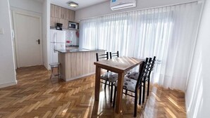Una cocina compacta con electrodomésticos modernos, una mesa de comedor con sillas y un amplio ventanal con cortinas translúcidas.