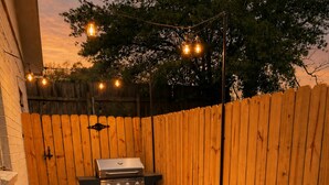 A backyard with a barbecue grill, two white chairs, and a fire pit. - Firethorn: Medical District, Summerville Cottage (Augusta)