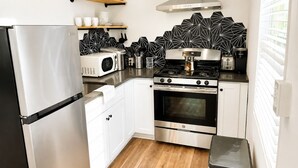 A compact kitchen with a refrigerator, microwave, stove, oven, and a coffee maker. - Firethorn: Medical District, Summerville Cottage (Augusta)