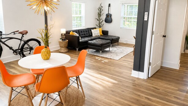 A modern living room with a dining area, a black sofa, a guitar, and a bicycle. - Firethorn: Medical District, Summerville Cottage (Augusta)