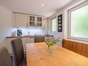 A modern kitchen with white cabinets, a wooden dining table, and a window with frosted glass. - Two bungalows with their own jetty 5 minutes from the lake (Rheinsberg)