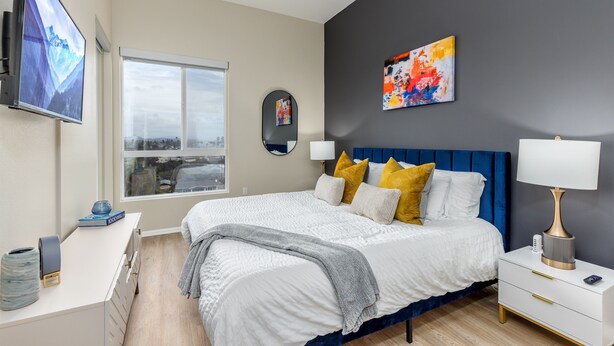 Un dormitorio moderno con una cama grande, mesitas de noche, un televisor y vistas a la ciudad.