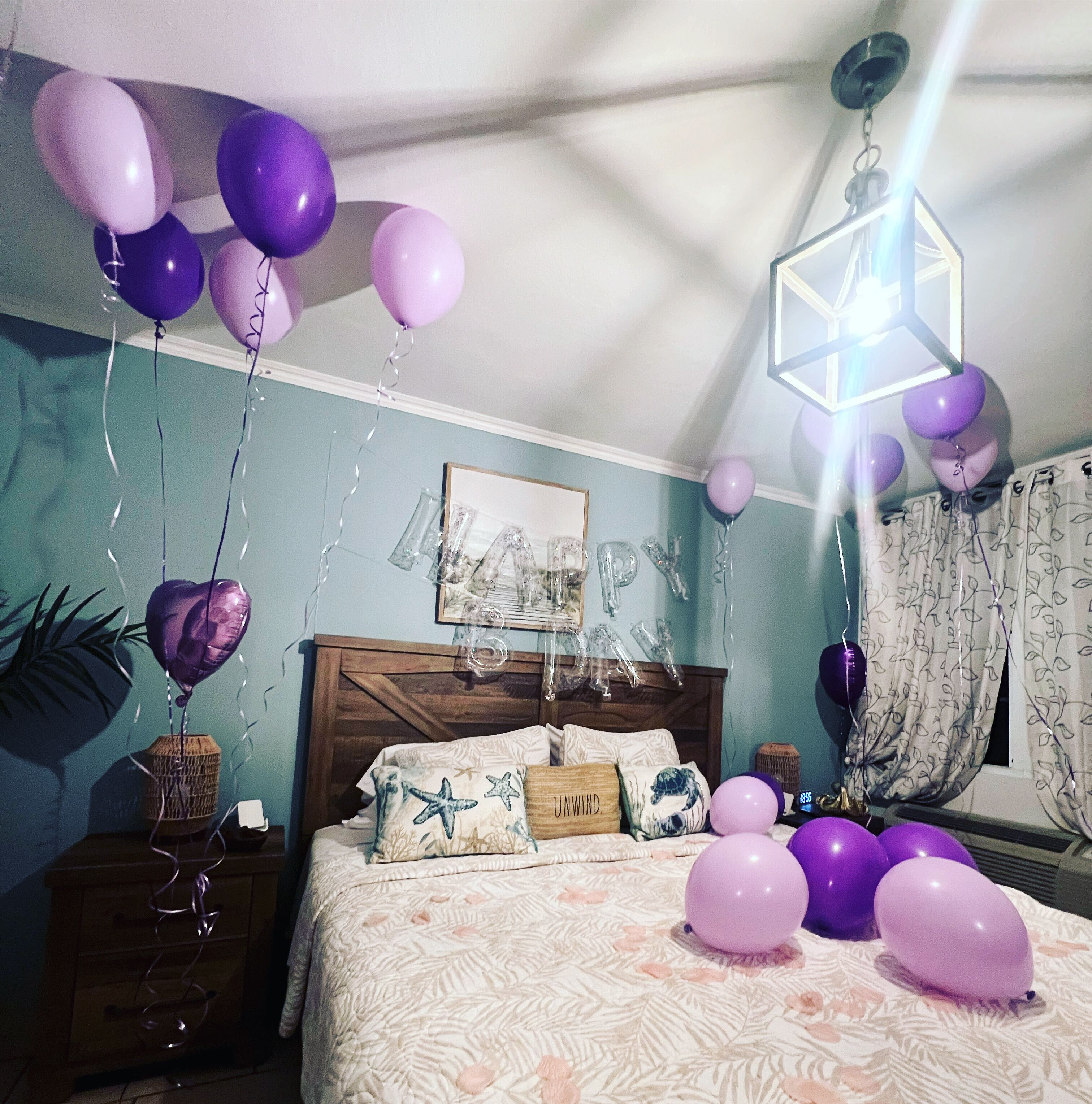 Un dormitorio con cama, almohadas, una mesita de noche, una lámpara colgante y globos.