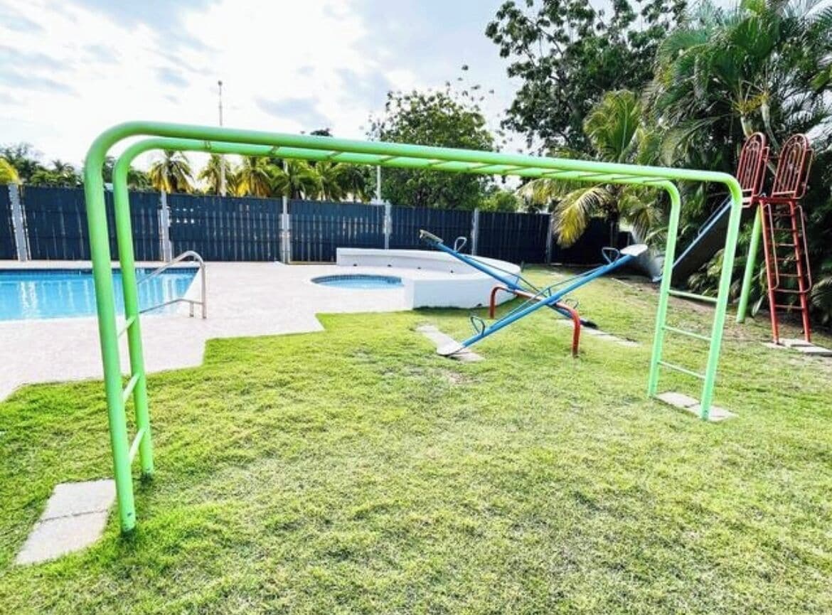 A backyard with a swimming pool, a green metal swing set, and a small circular hot tub.