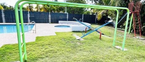A backyard with a swimming pool, a green metal swing set, and a small circular hot tub.