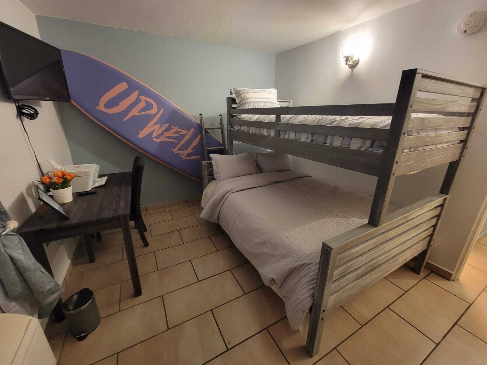 Habitación con literas, un escritorio, una silla y un letrero que dice 'UP WELL'.