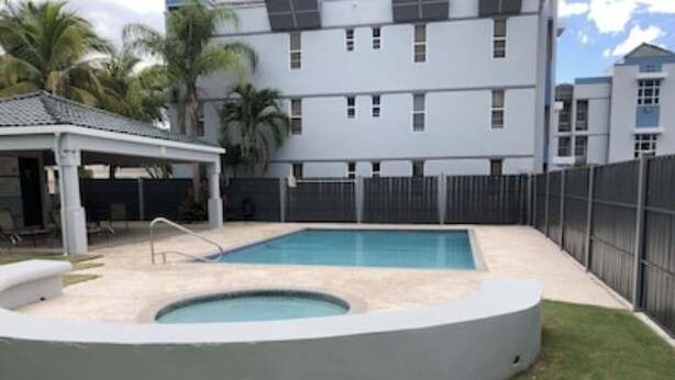 Una piscina con un jacuzzi circular, una zona de estar cubierta y un patio trasero cercado.