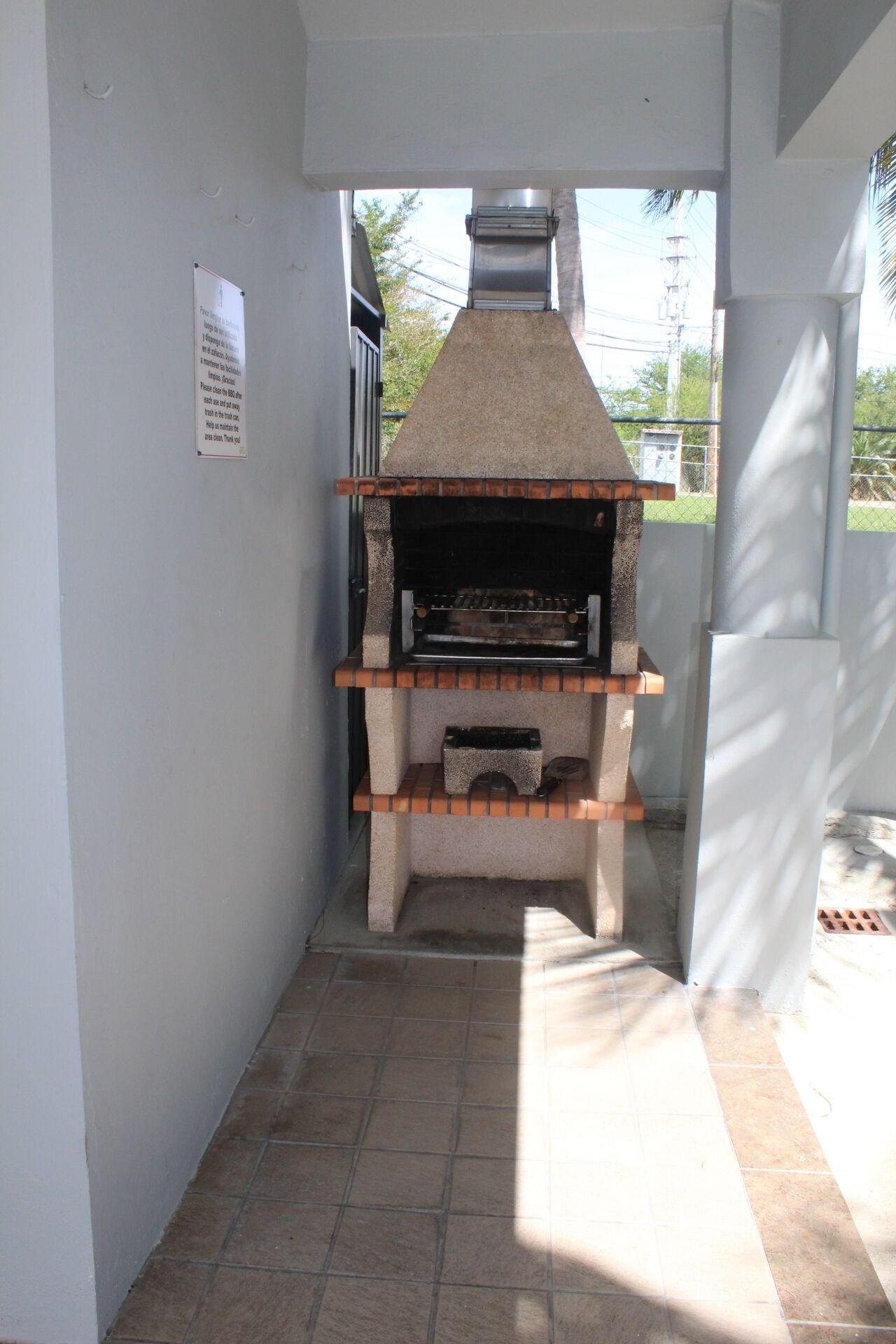 Een kleine, in baksteen opgemetselde oven met schoorsteen, in een smalle ruimte met betegelde vloer en witte muren.
